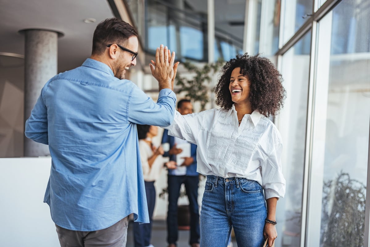 Two happy business colleagues give a high five in a bright office, celebrating success and teamwork